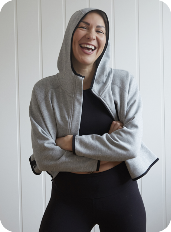 A woman in a grey hoody laughing with her arms folded